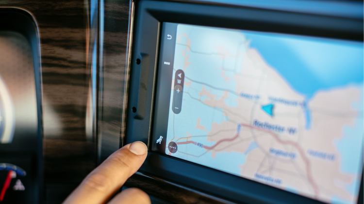 Close-up of a Mack truck's touchscreen navigation system displaying a map, with a hand selecting an option