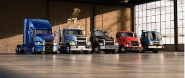 Lineup of five Mack Trucks in a showroom, featuring various models in blue, silver, black, red, and teal
