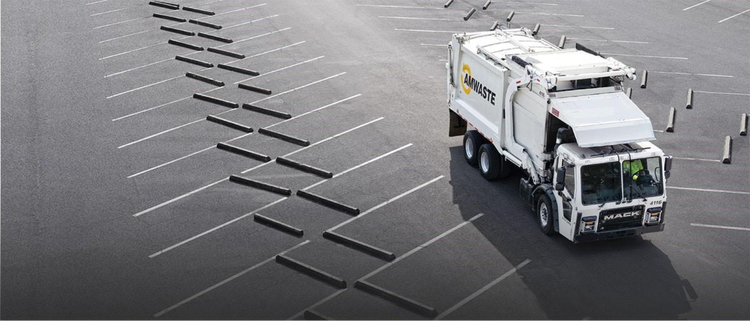 A white Mack garbage truck navigating through an empty parking lot