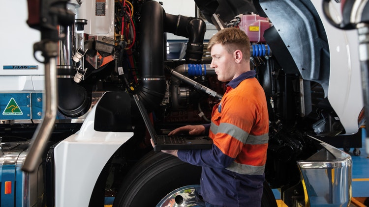 Technician diagnosing a Mack truck engine using a laptop, shows parts protection plan