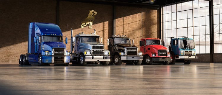 Lineup of Mack Trucks in various models and colors inside a showroom.