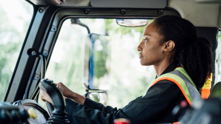 Closeup of a sideview of a driver holding the steering wheel, illustrating large windshield and mirrors.